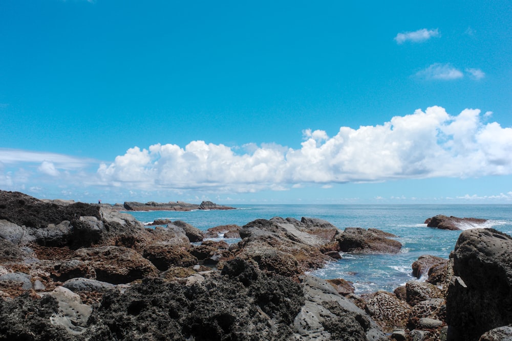 brown rock formation near sea under blue sky and white clouds during daytime