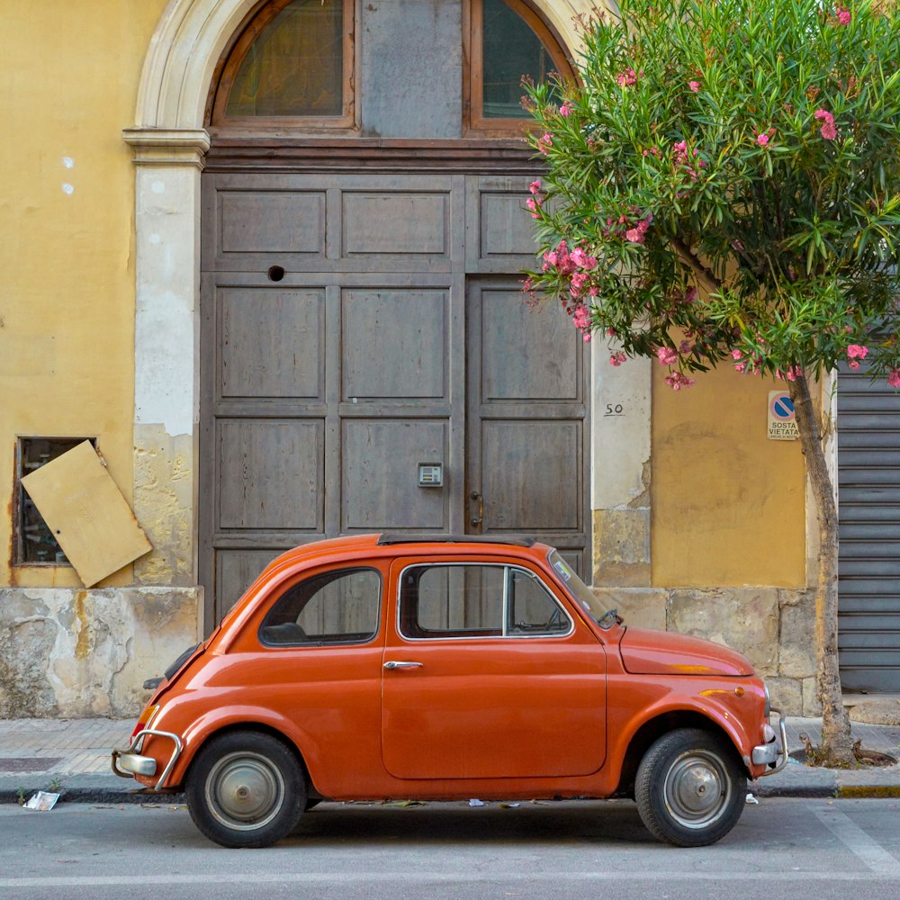 Volkswagen Beetle rojo estacionado junto a un edificio de concreto marrón durante el día