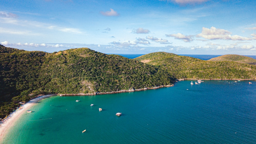 aerial view of boats on sea near green mountain under blue sky during daytime