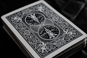 A close-up view of the backside of a deck of playing cards with intricate black and white designs, featuring floral patterns and symmetrical artwork.