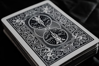 A close-up view of the backside of a deck of playing cards with intricate black and white designs, featuring floral patterns and symmetrical artwork.