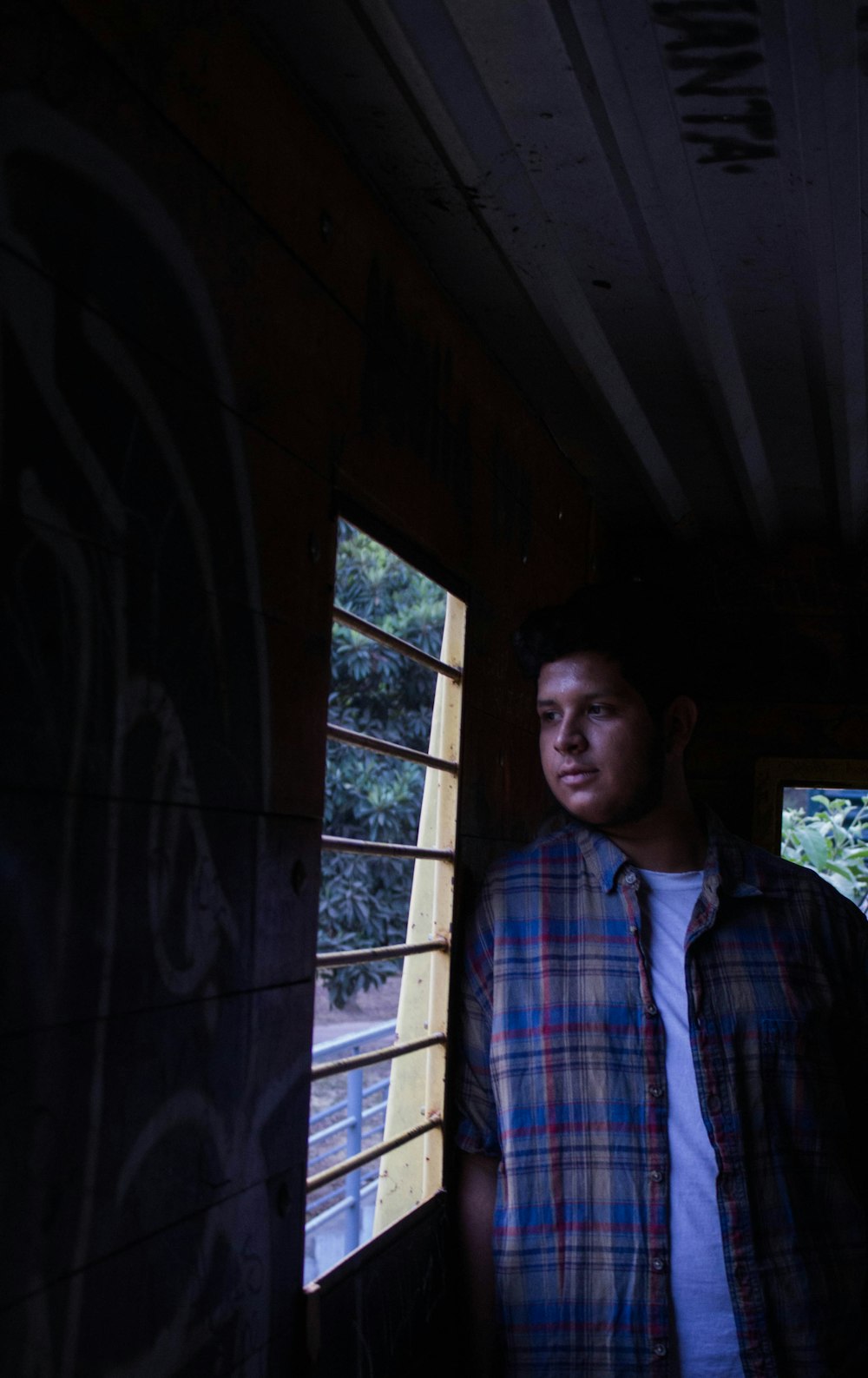 man in blue white and red plaid button up shirt standing near window