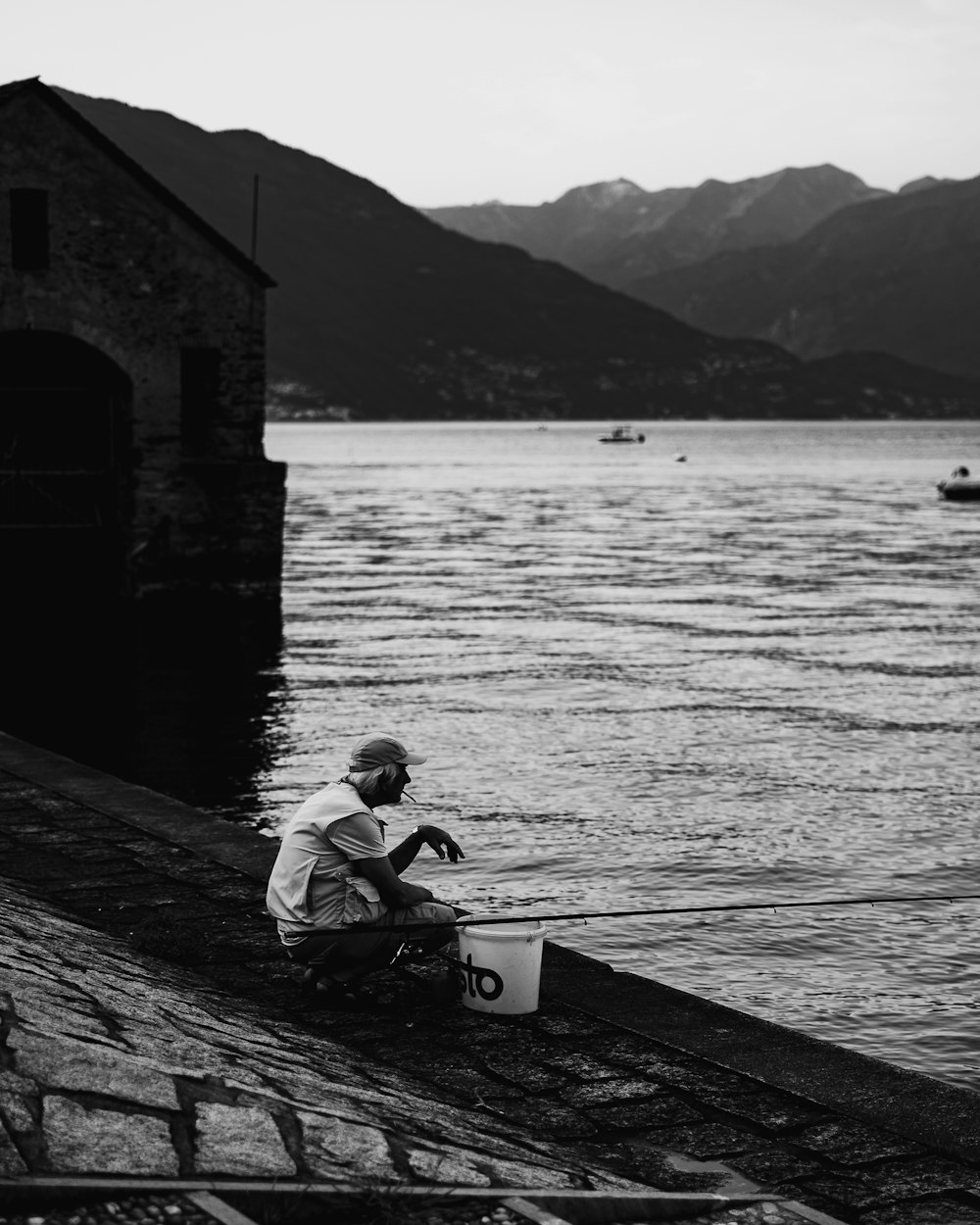 man in white shirt sitting on wooden dock in grayscale photography