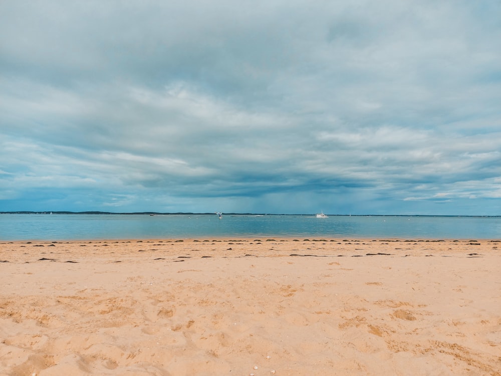 brown sand near body of water under white clouds during daytime