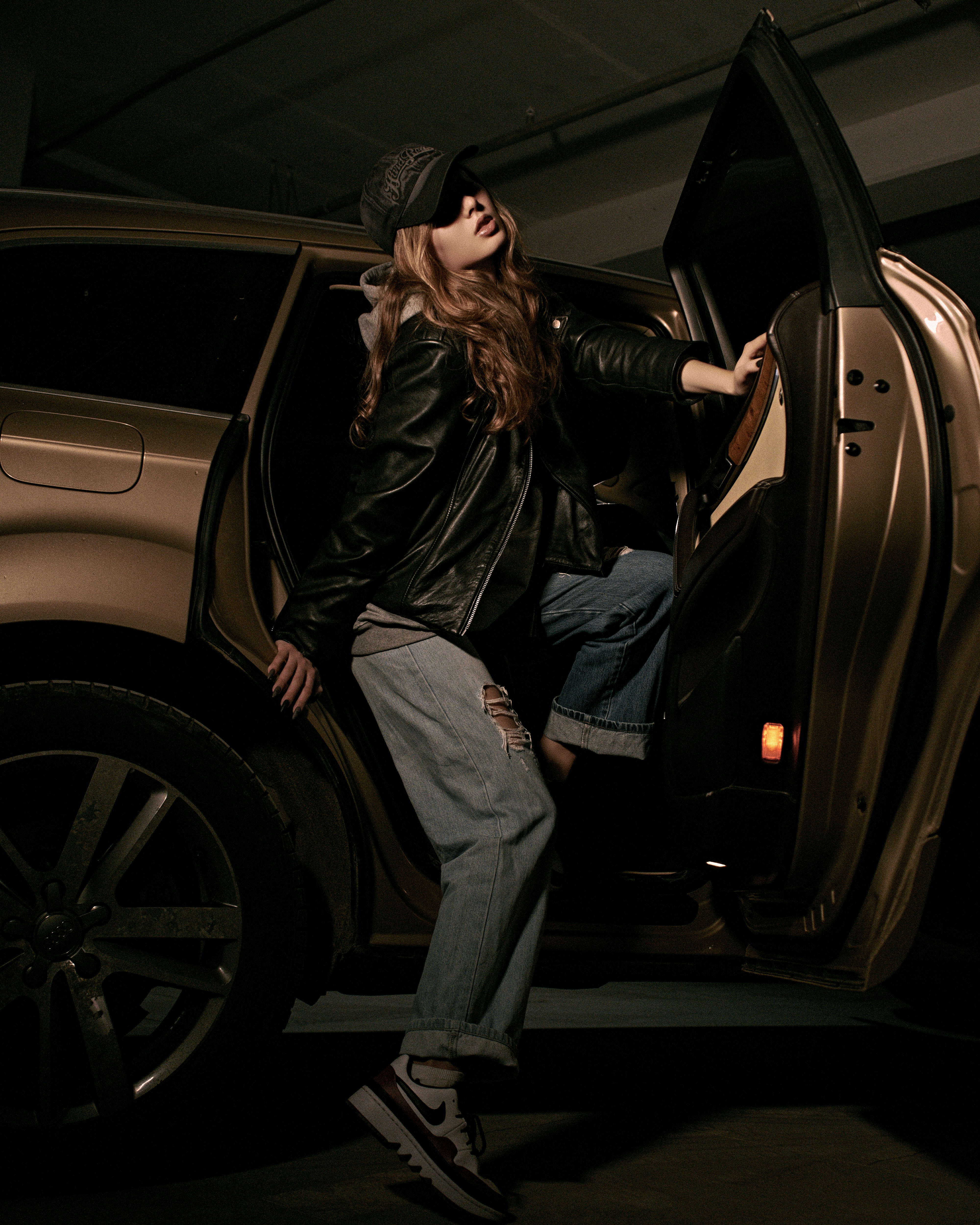man in black leather jacket and blue denim jeans leaning on black car