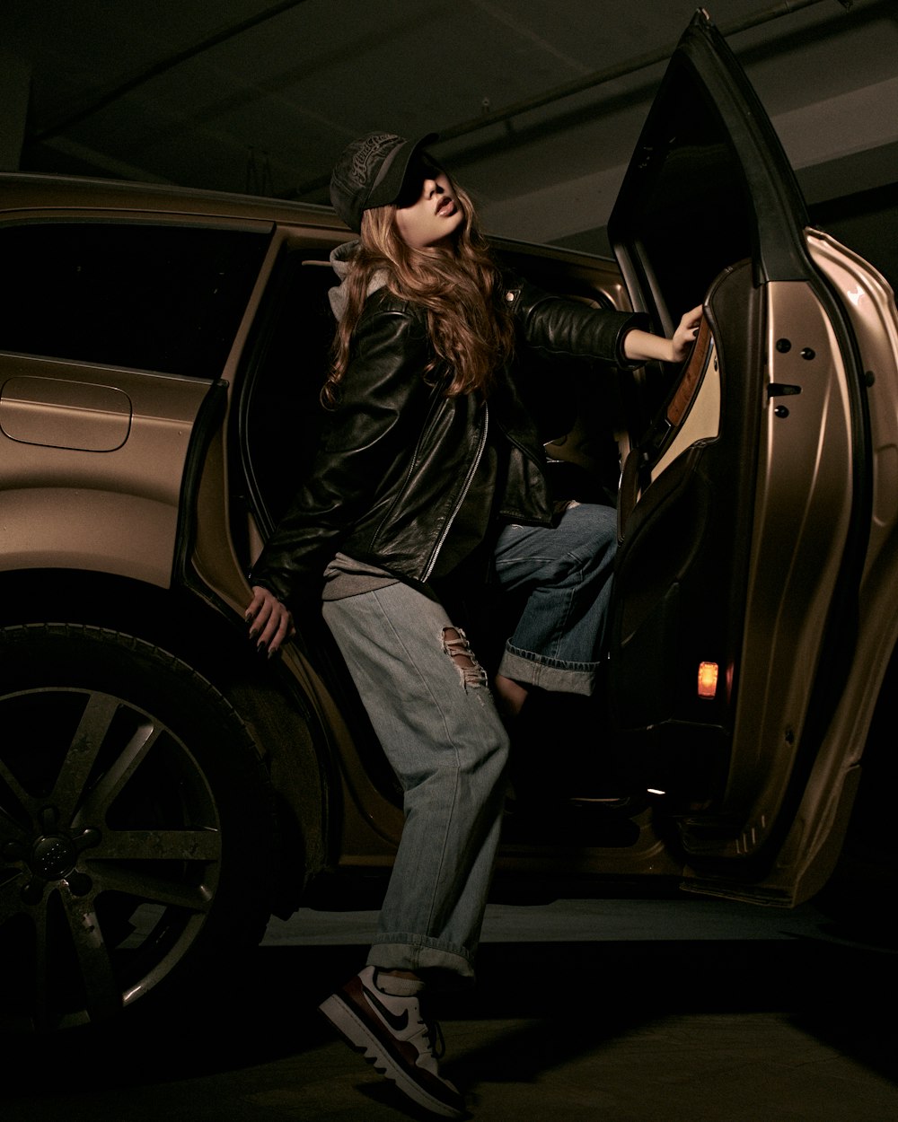 man in black leather jacket and blue denim jeans leaning on black car