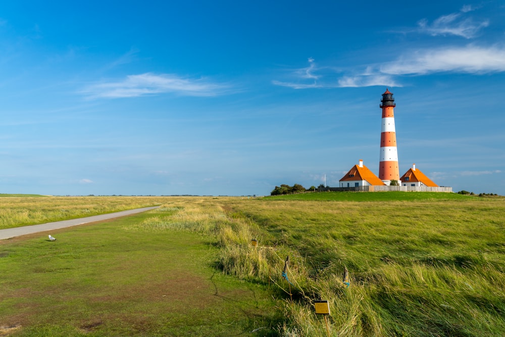 white and red lighthouse on green grass field under blue sky during daytime