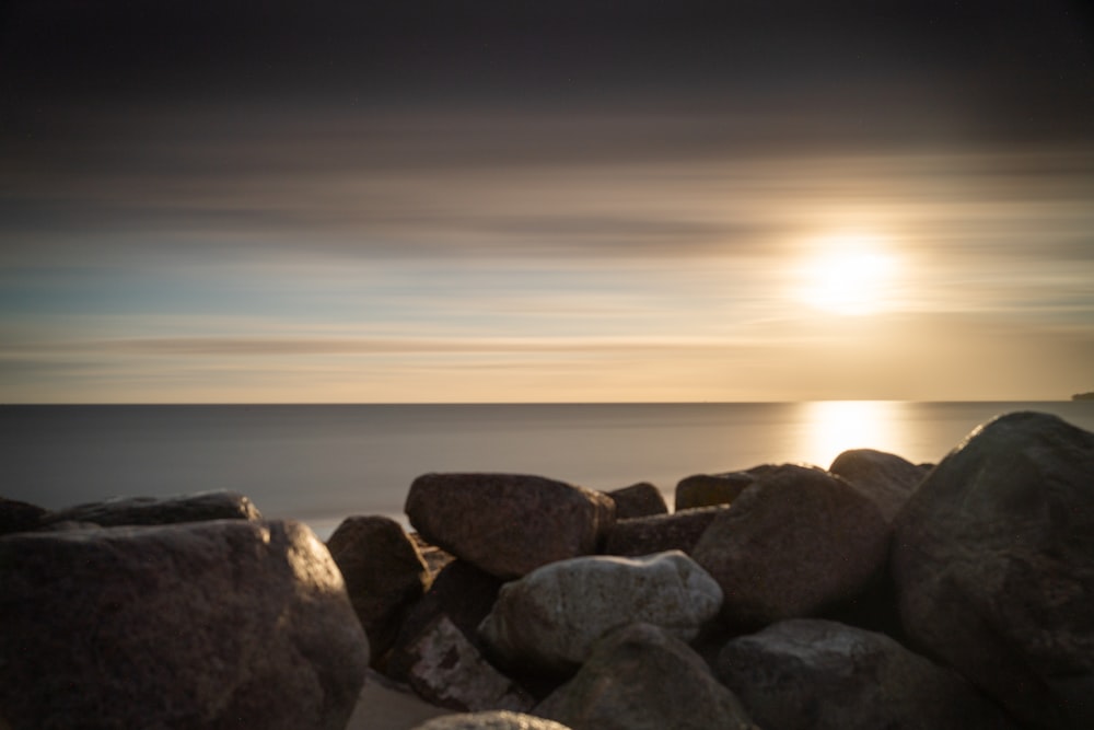 the sun is setting over the ocean and rocks