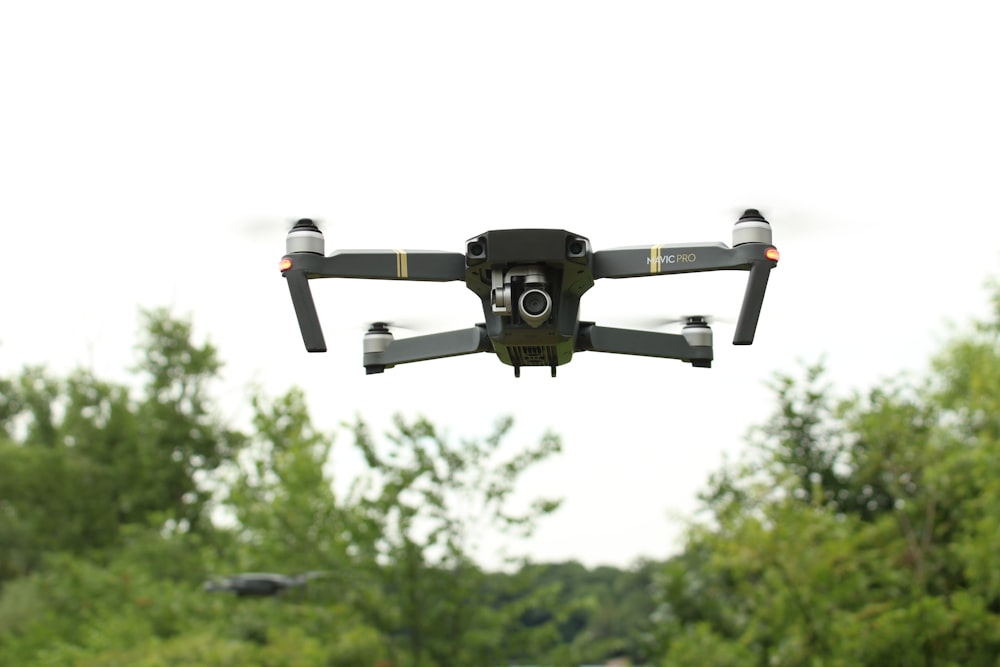 black and gray drone flying over green trees during daytime