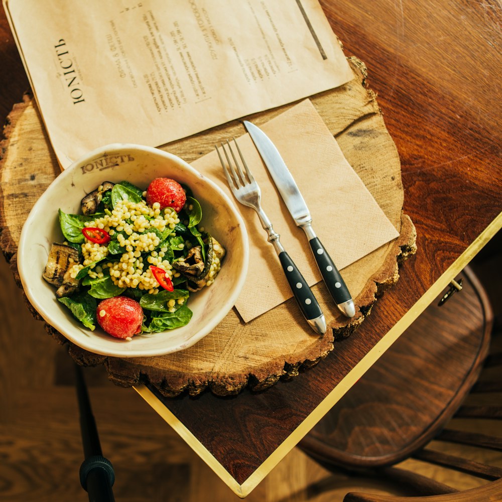vegetable salad on white ceramic bowl beside stainless steel fork and knife
