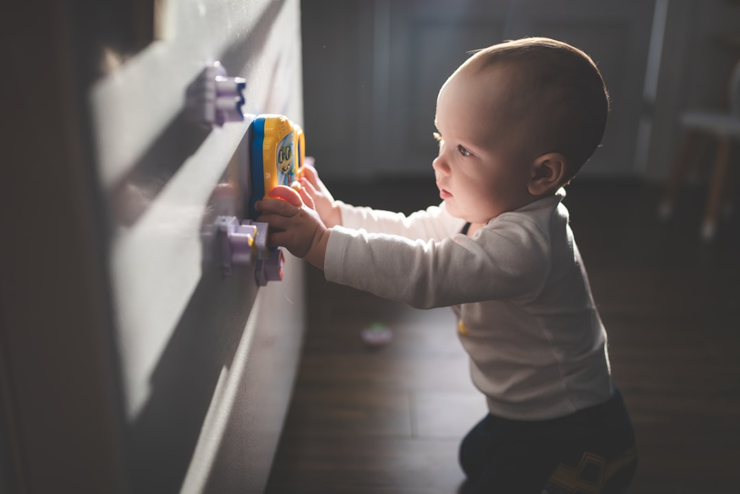 baby in white long sleeve shirt and black pants holding blue plastic toy