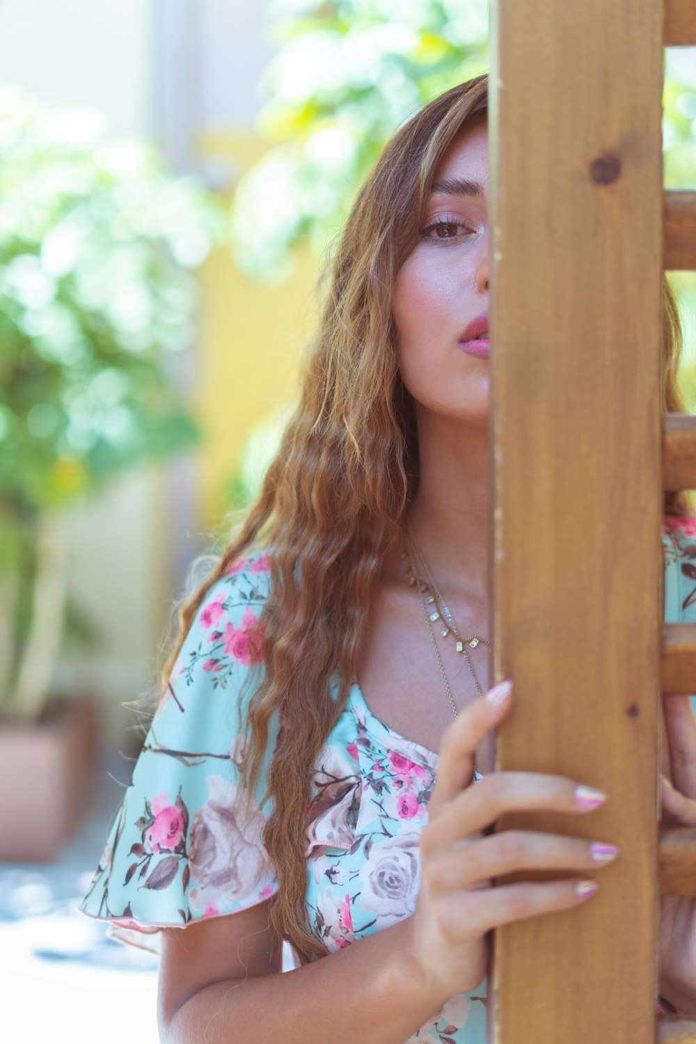 woman in white and pink floral shirt leaning on brown wooden fence