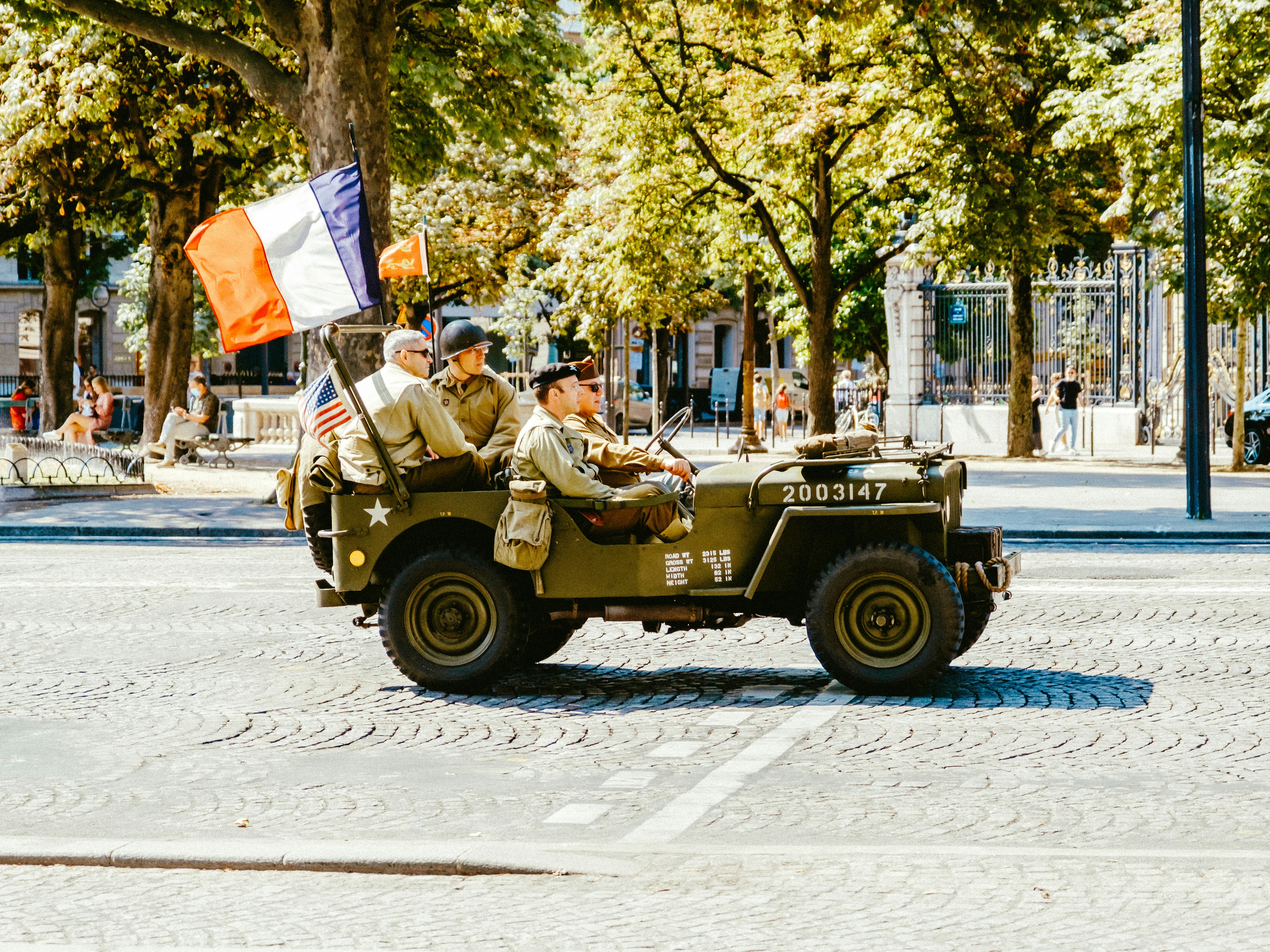 3 men riding on green and brown camouflage vehicle on road during daytime