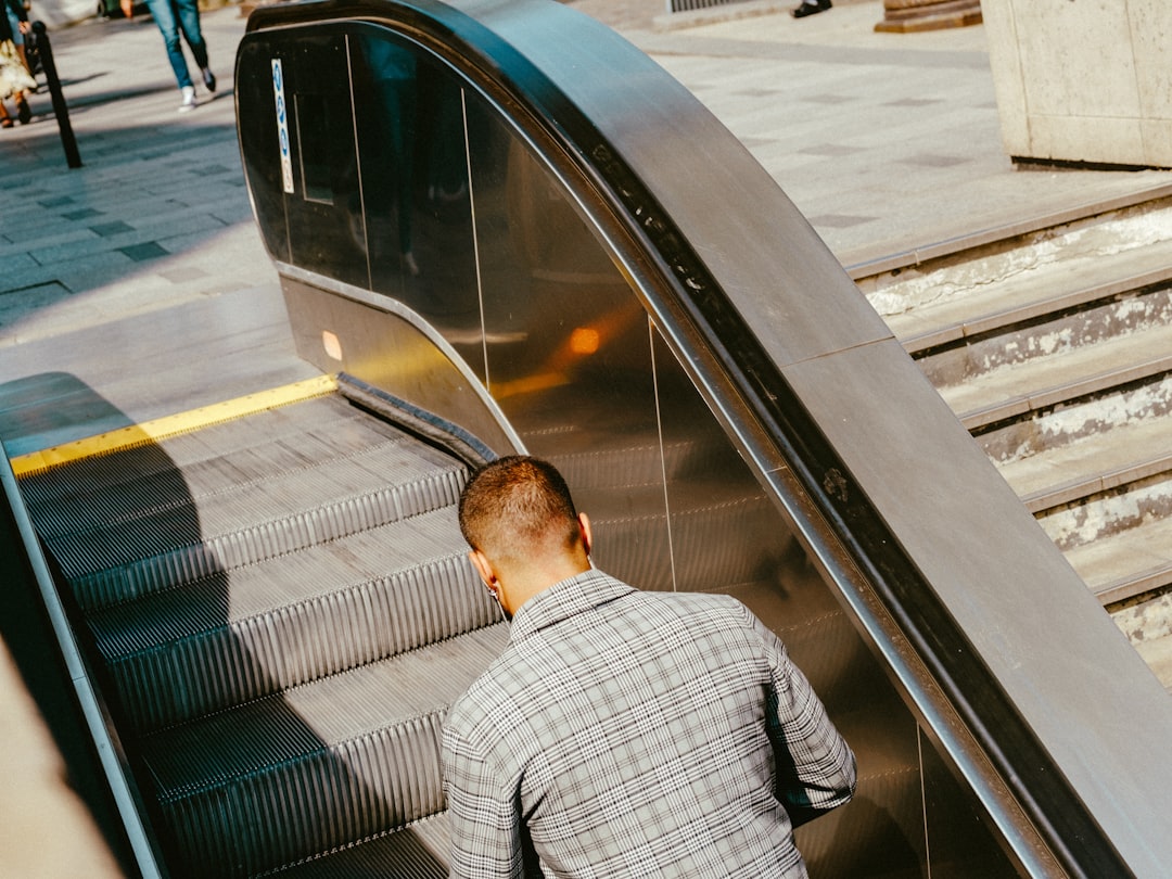 man in gray and white plaid dress shirt standing beside train rail during daytime