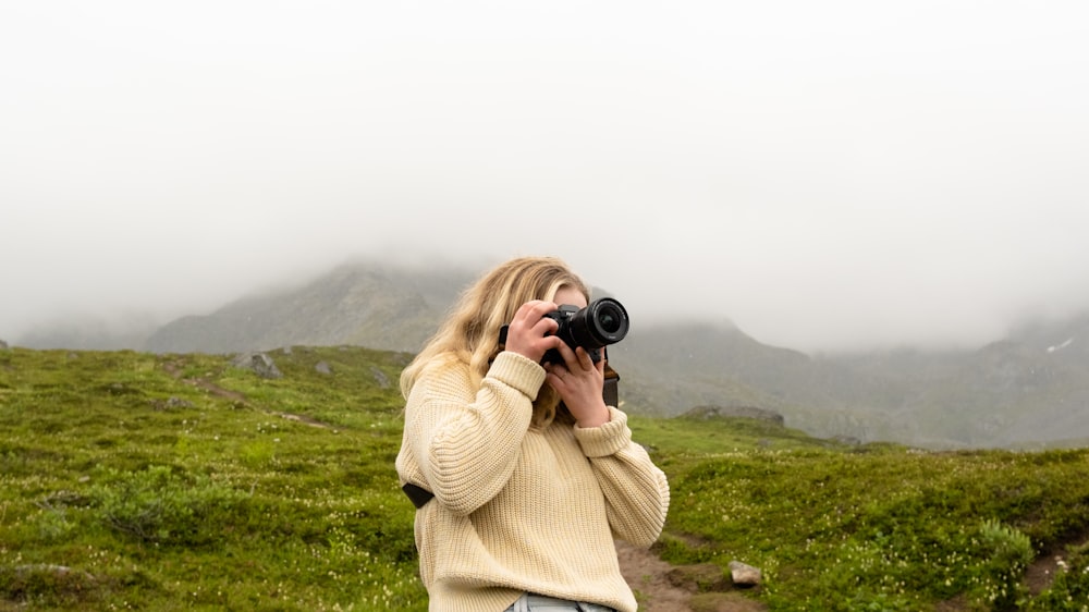 woman in beige sweater holding black dslr camera