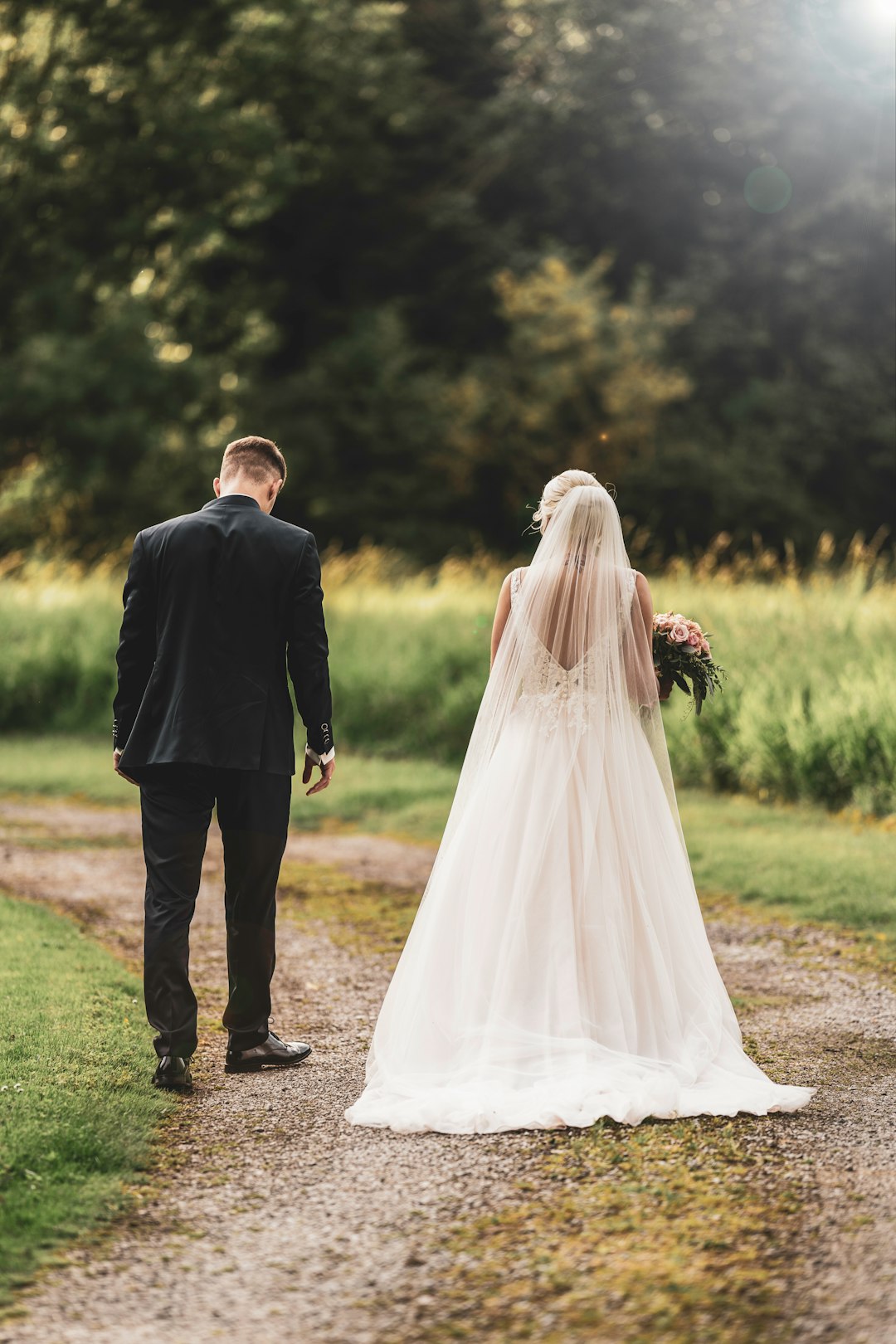 man in black suit and woman in white wedding dress walking on green grass field during