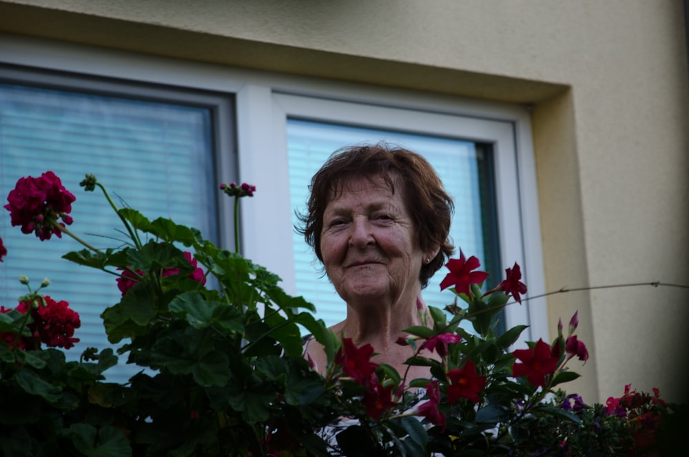 woman in red shirt standing beside red flowers