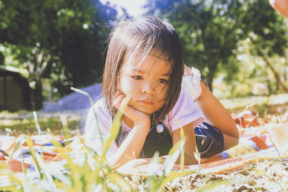 girl in white and blue dress sitting on orange and blue textile on green grass field