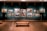 A dimly lit art gallery displays an array of classical paintings, each framed in ornate gold, hung against a teal wall. The floor features polished wood, and there is a simple wooden bench in the foreground. The paintings depict various historical or architectural scenes.