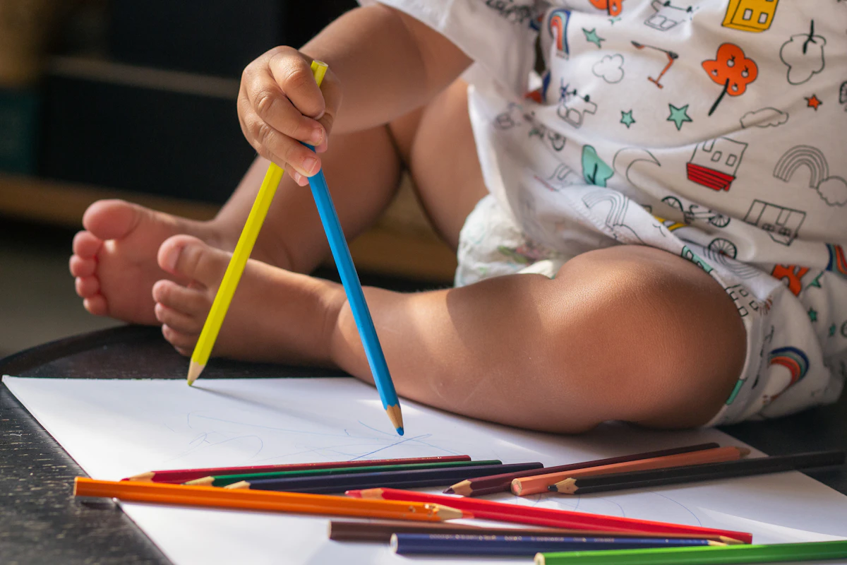 Toddler holding two pencils near a sheet of paper