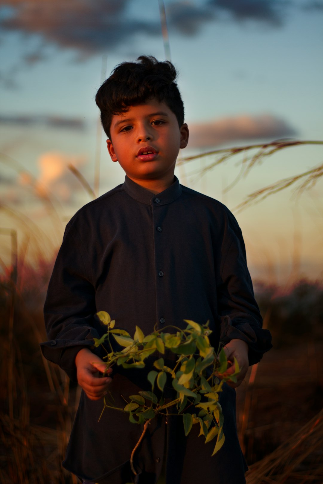 boy in black button up long sleeve shirt holding green plant during daytime