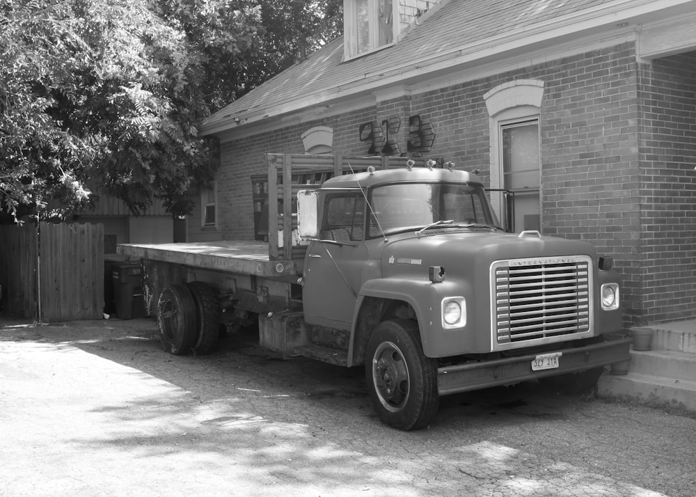 grayscale photo of truck in front of wooden house