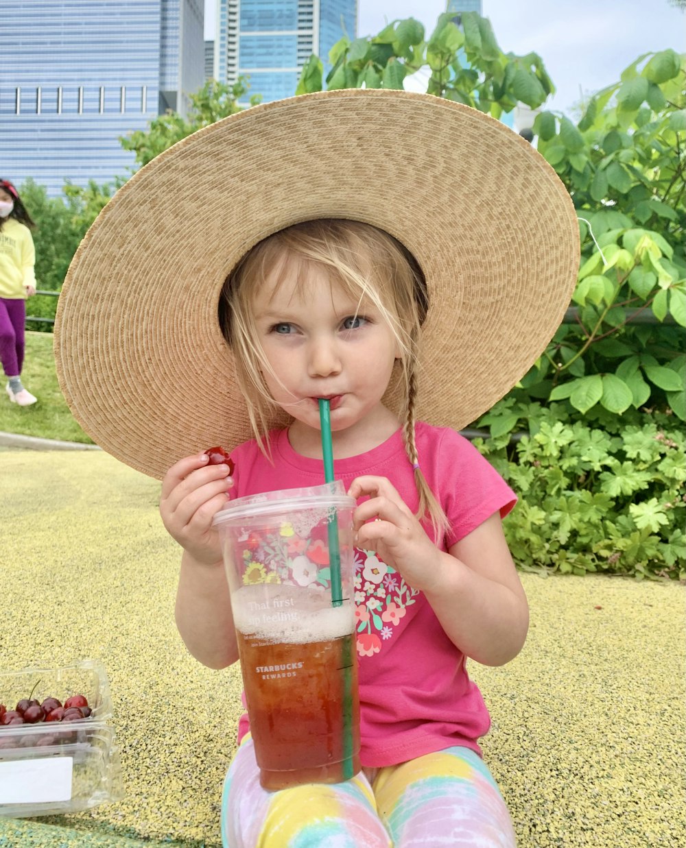 girl in pink shirt holding clear plastic cup with straw