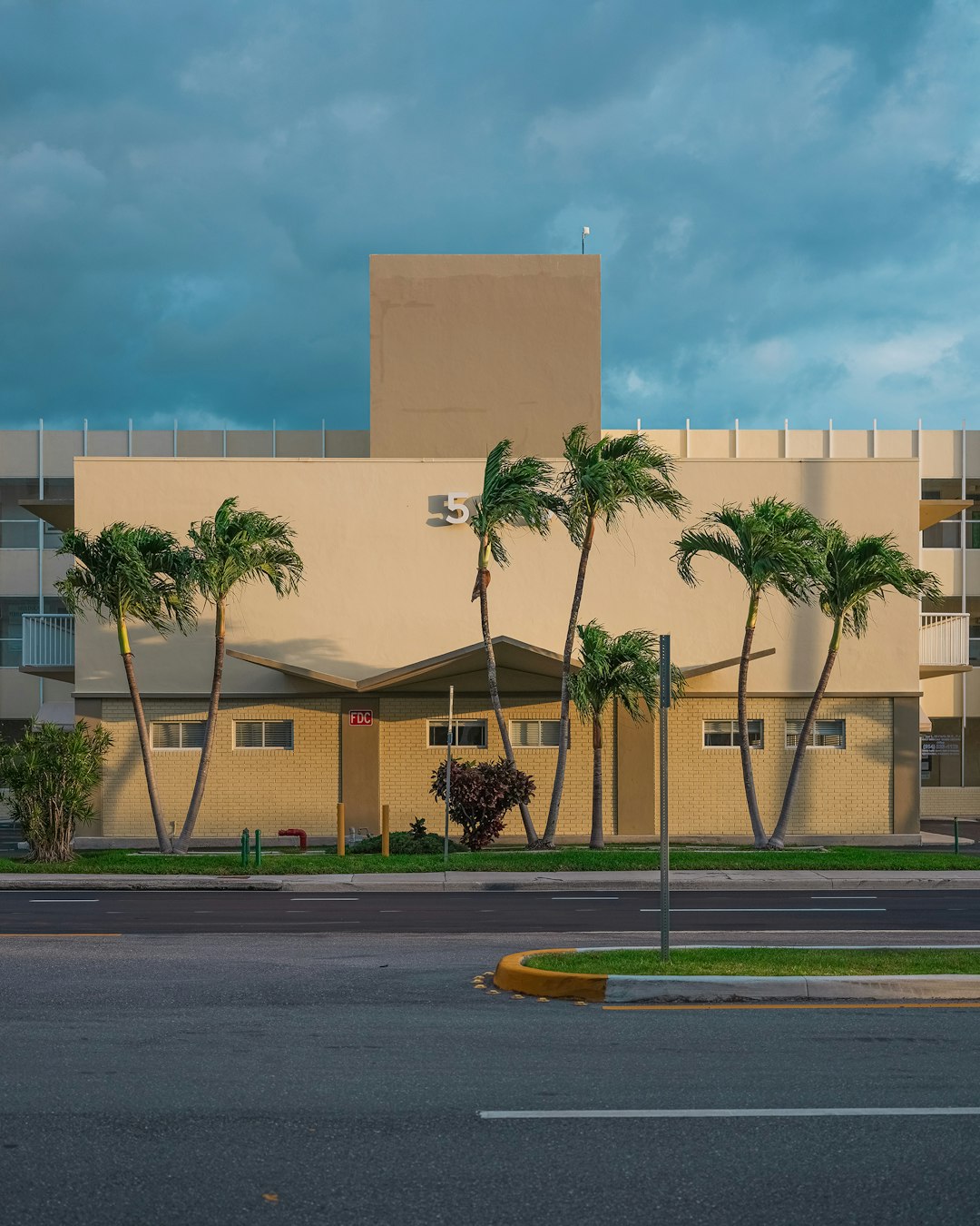 beige concrete building near green trees under white clouds during daytime