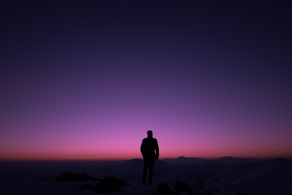 silhouette of man standing on rock formation during sunset