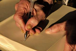 A close-up of Harry's weathered hands holding a worn notebook filled with handwritten notes and sketches.