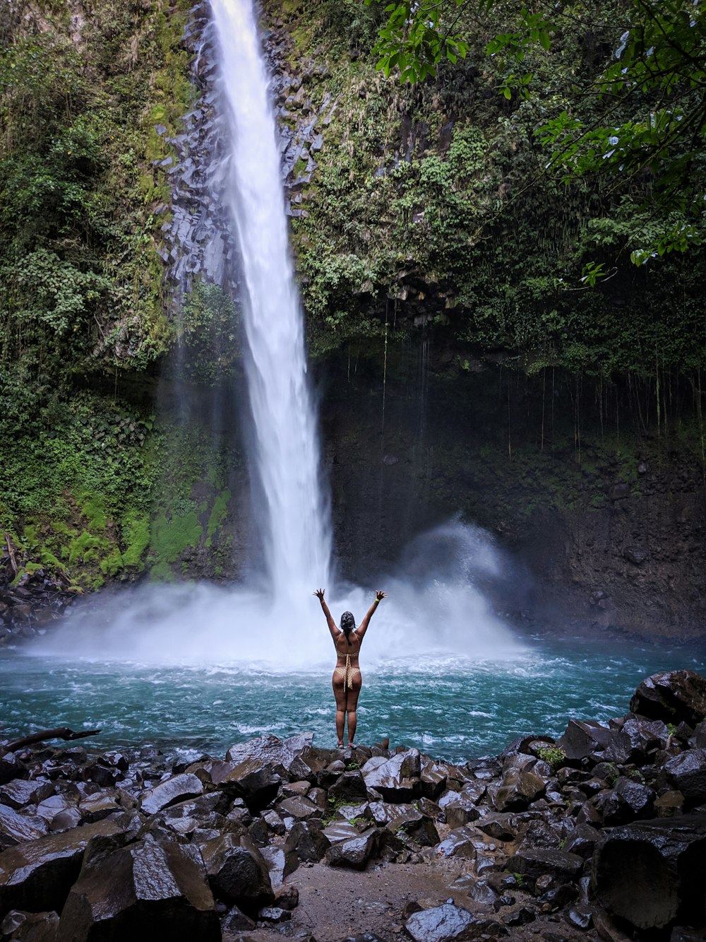 man standing on rocky shore near waterfalls during daytime