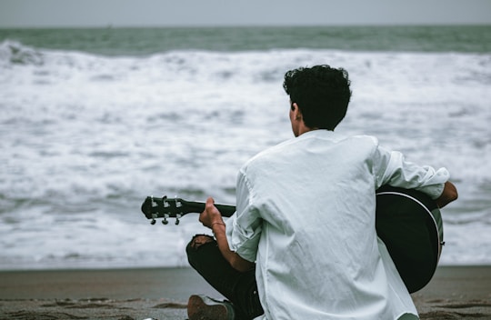 man in white dress shirt and black pants sitting on brown rock near sea during daytime