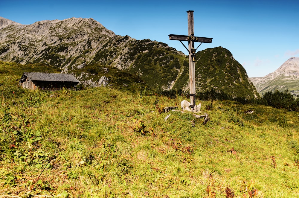 brown wooden cross on green grass field near gray rocky mountain under blue sky during daytime