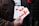 A person is holding several pamphlets with a large red cross design on them. The text on the pamphlets includes 'THE CROSS OF LOVE.' The individual is wearing a brown jacket, and the background is blurred, suggesting an outdoor environment.