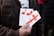 A person is holding several pamphlets with a large red cross design on them. The text on the pamphlets includes 'THE CROSS OF LOVE.' The individual is wearing a brown jacket, and the background is blurred, suggesting an outdoor environment.