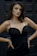 A stylish woman wearing a sleek black dress from Auradourada, smiling confidently in a minimalist setting.