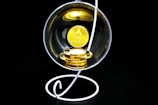 A stack of gold-colored Ethereum coins placed inside a transparent spherical container held by a white, spiral stand on a black background.