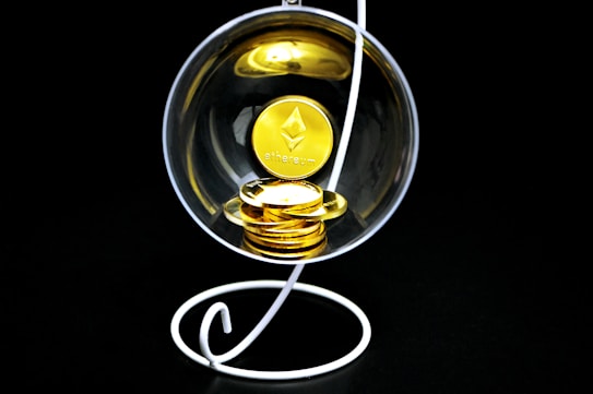 A stack of gold-colored Ethereum coins placed inside a transparent spherical container held by a white, spiral stand on a black background.