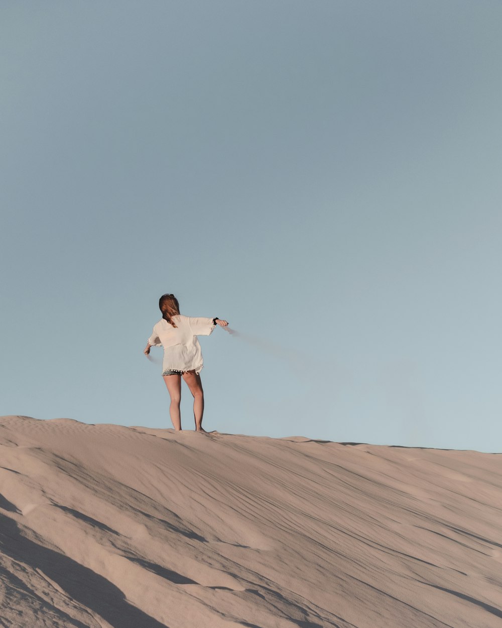 Frau in weißem Hemd und weißen Shorts, die tagsüber auf braunem Sand steht