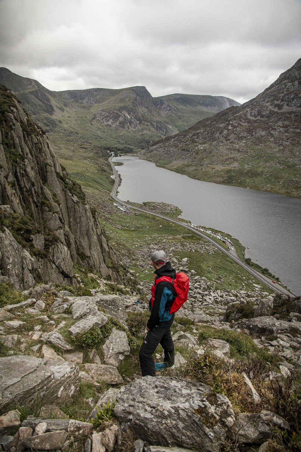 person in red jacket and black pants walking on rocky road near body of water during