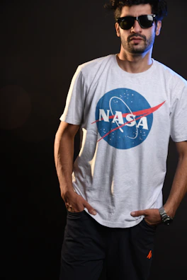 Model wearing a minimalist black t-shirt featuring an astronaut silhouette against a dark urban backdrop.