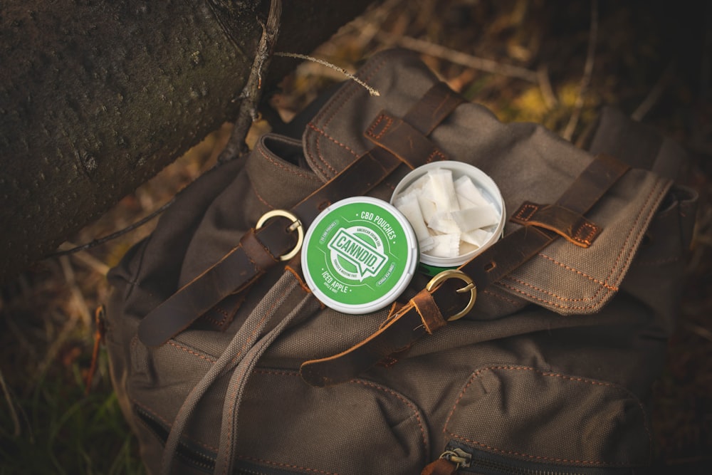 green and white round container on black leather bag