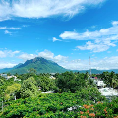 A lush green mountain landscape in Jarabacoa with scattered plots of land under a bright blue sky.