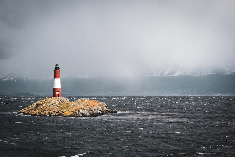 red and white lighthouse on brown rock formation near body of water