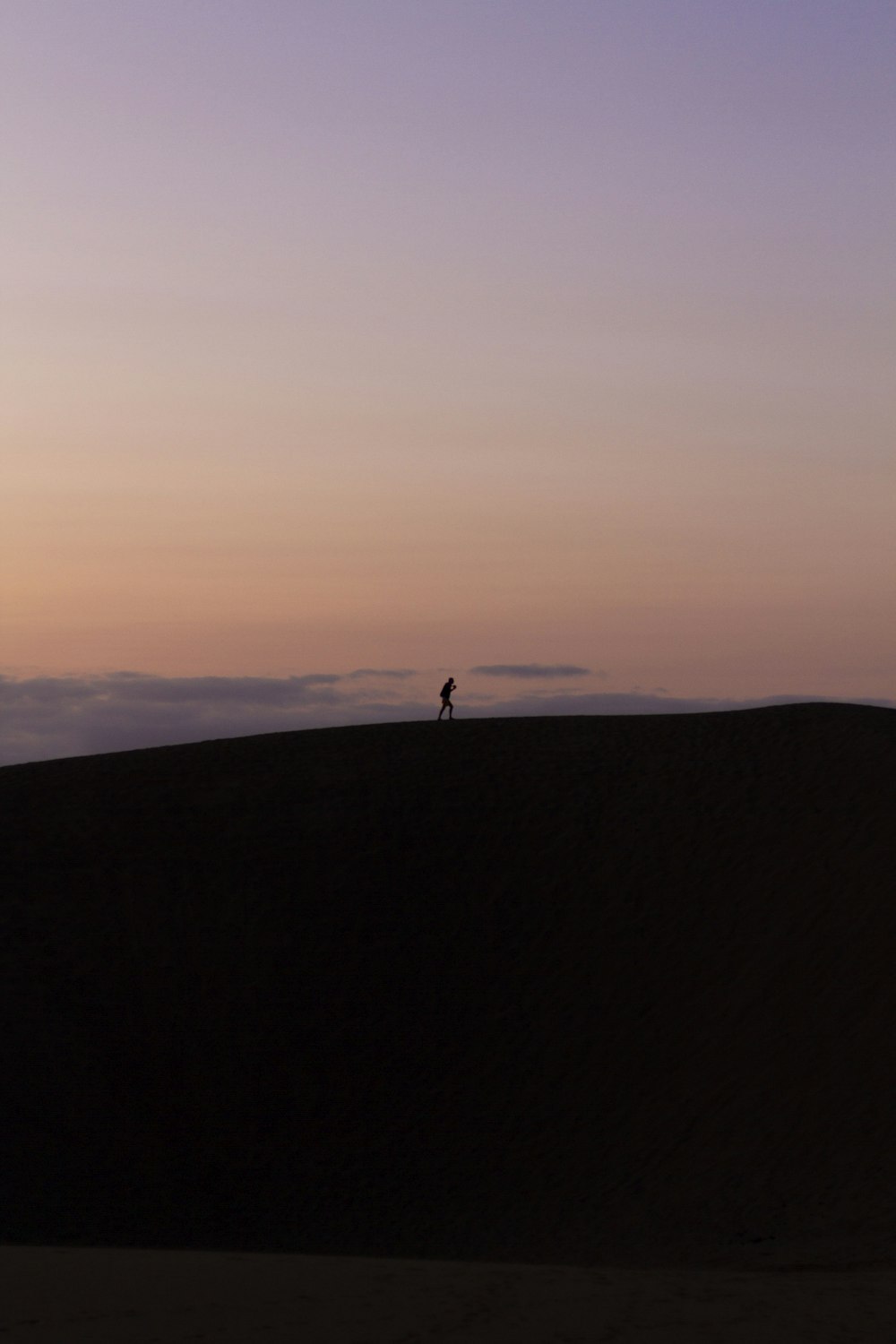 silhouette of person standing on hill during sunset