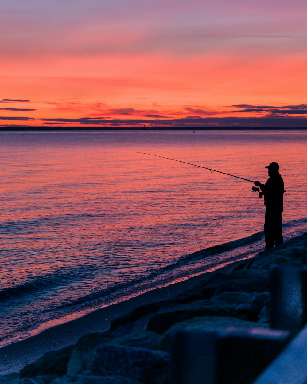 silhouette of man fishing on sea during sunset