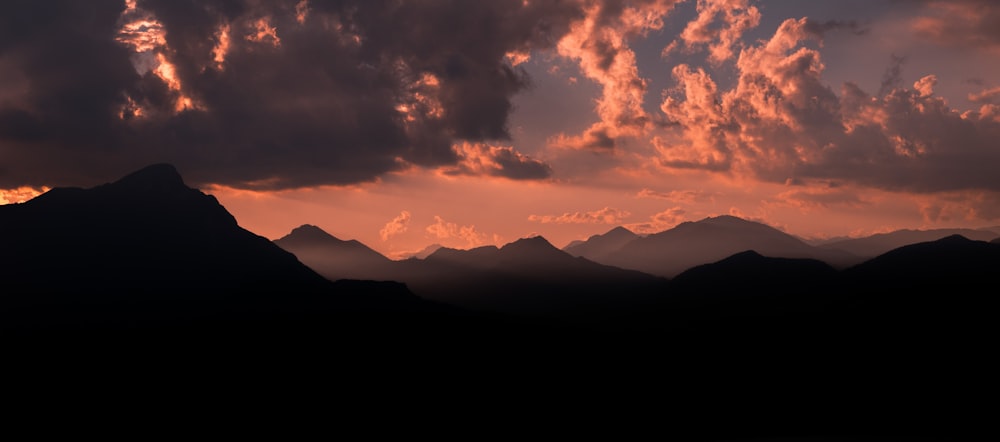 silhouette of mountains under cloudy sky during sunset