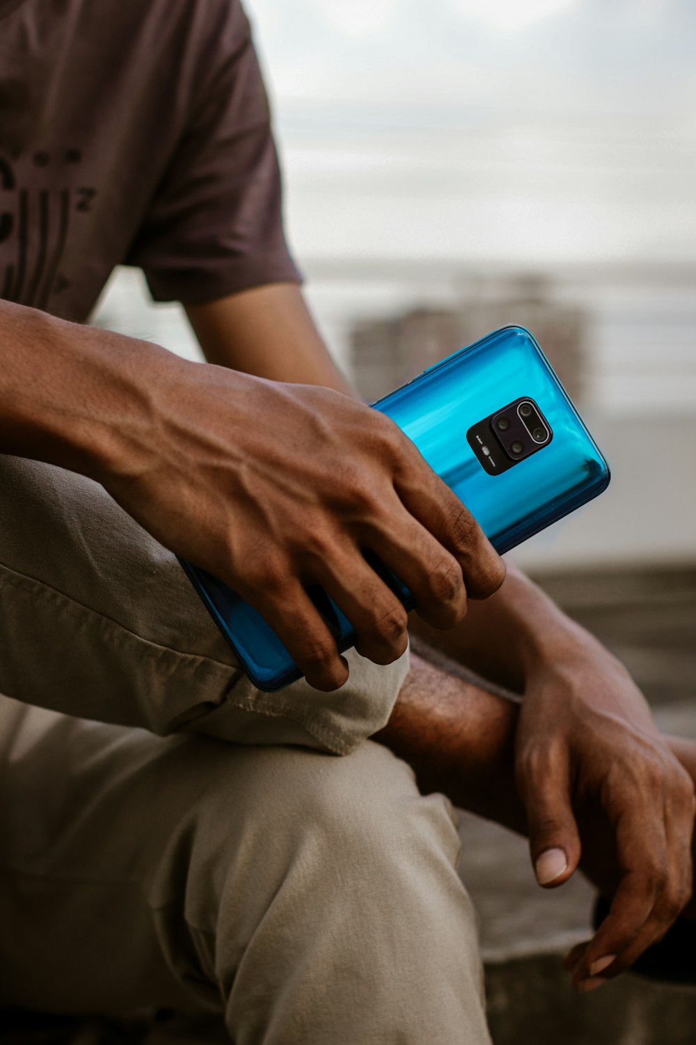 pessoa em calças cinza segurando smartphone azul