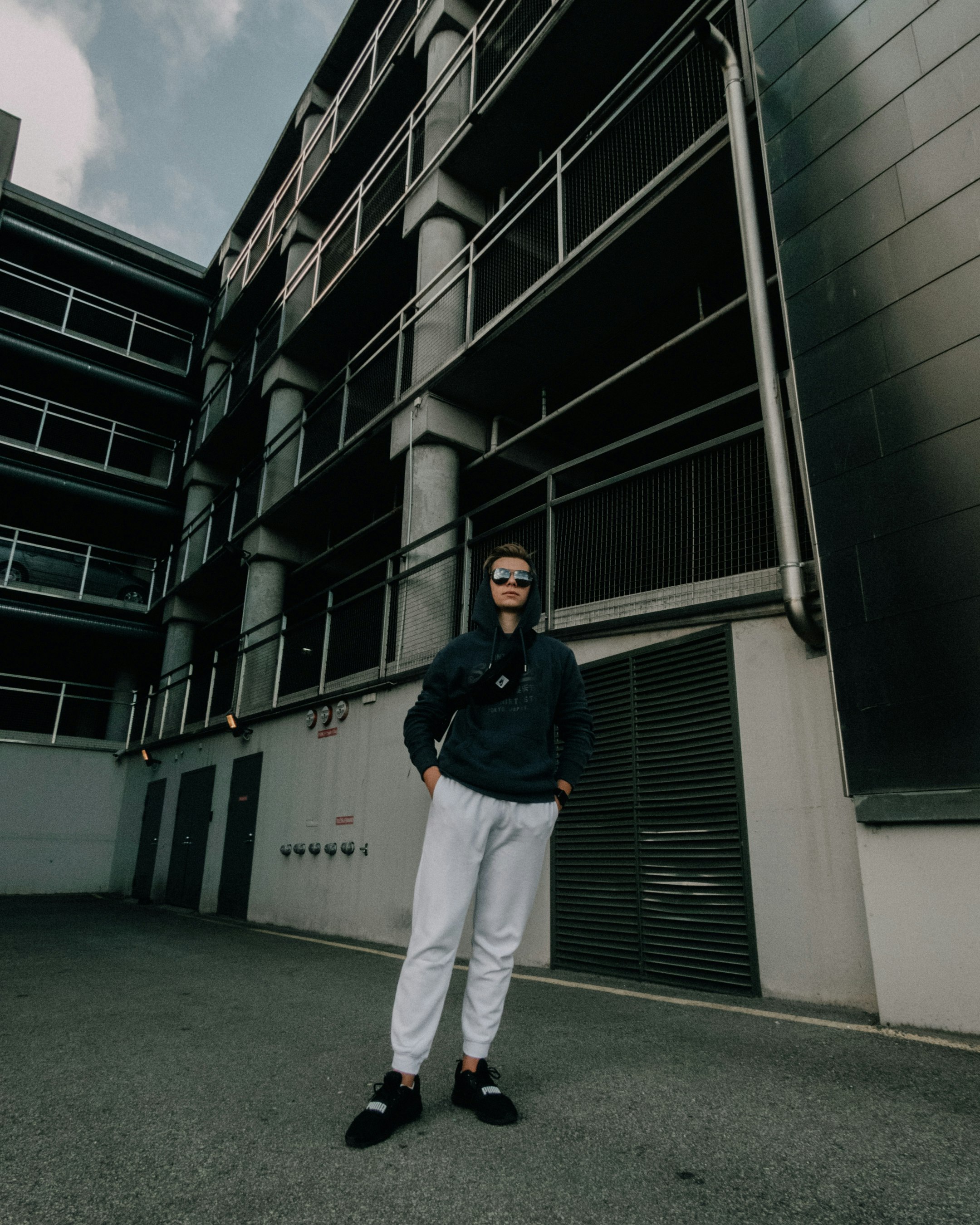 man in black jacket and white pants standing on gray concrete floor