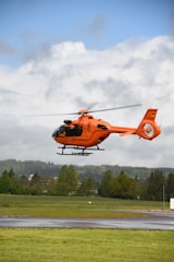 orange helicopter flying over green trees during daytime